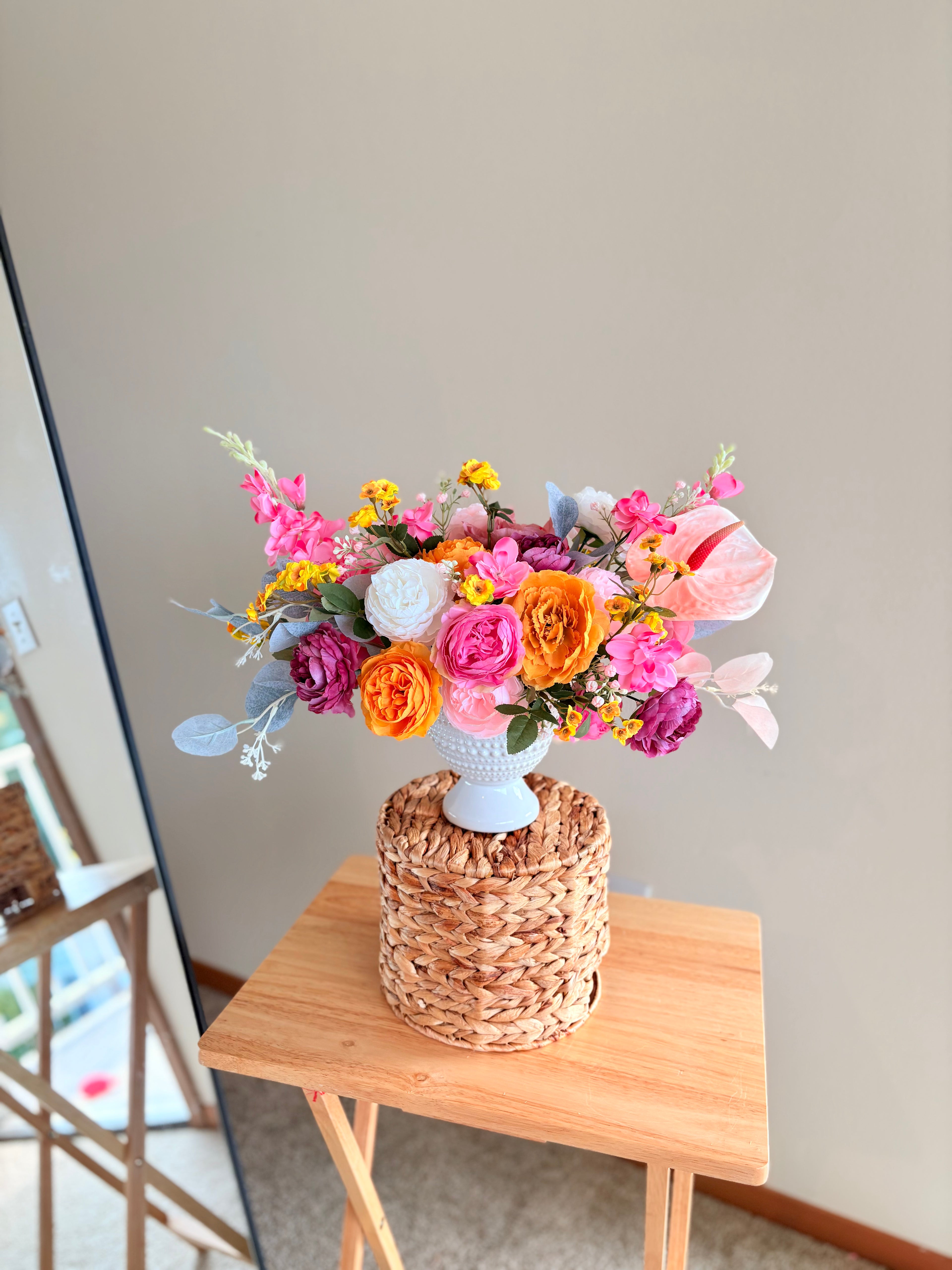 Colorful flower arrangement in a white vase on a wooden table with a light gray background