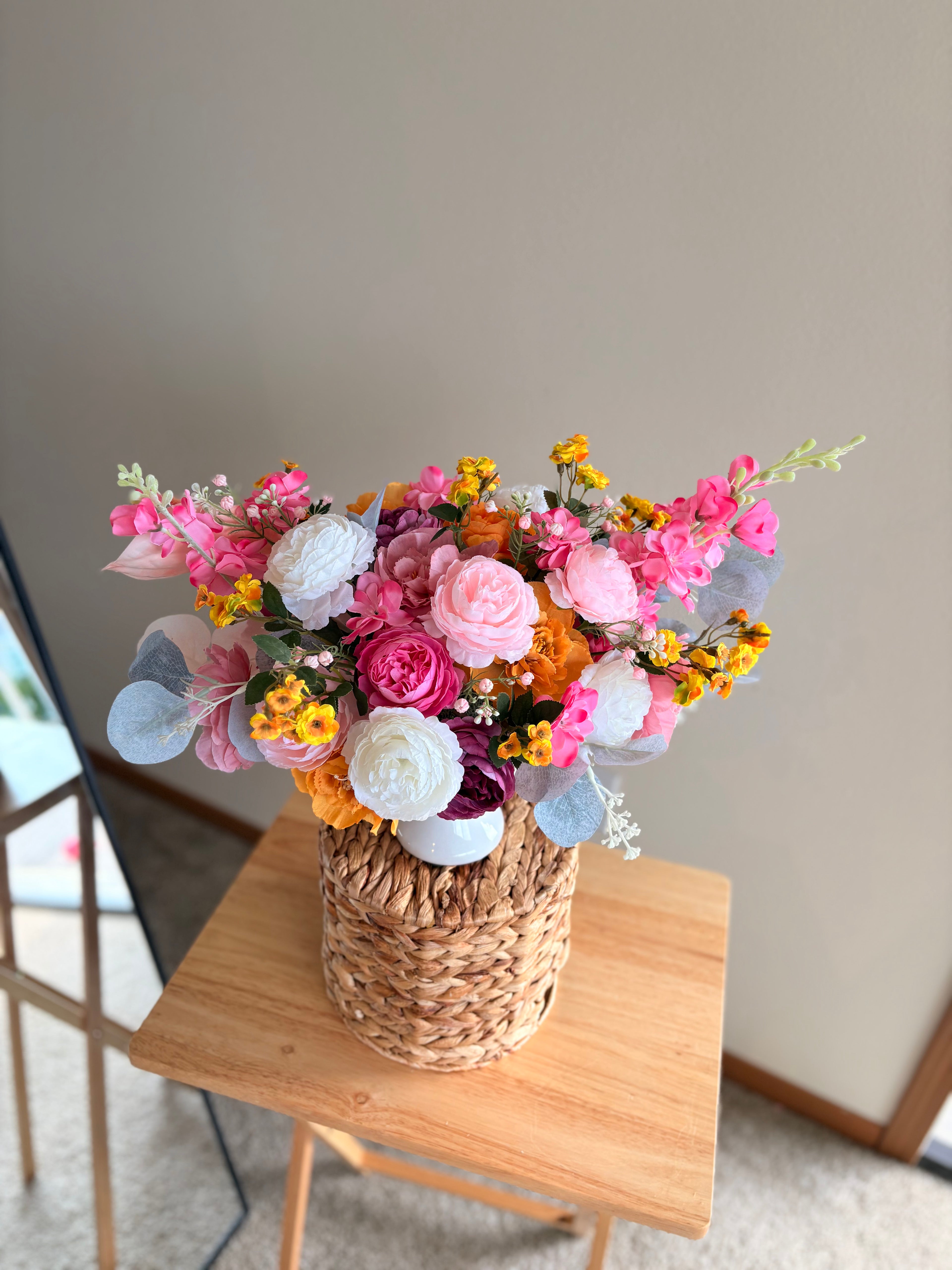 Bouquet of colorful flowers in a woven basket on a wooden table.
