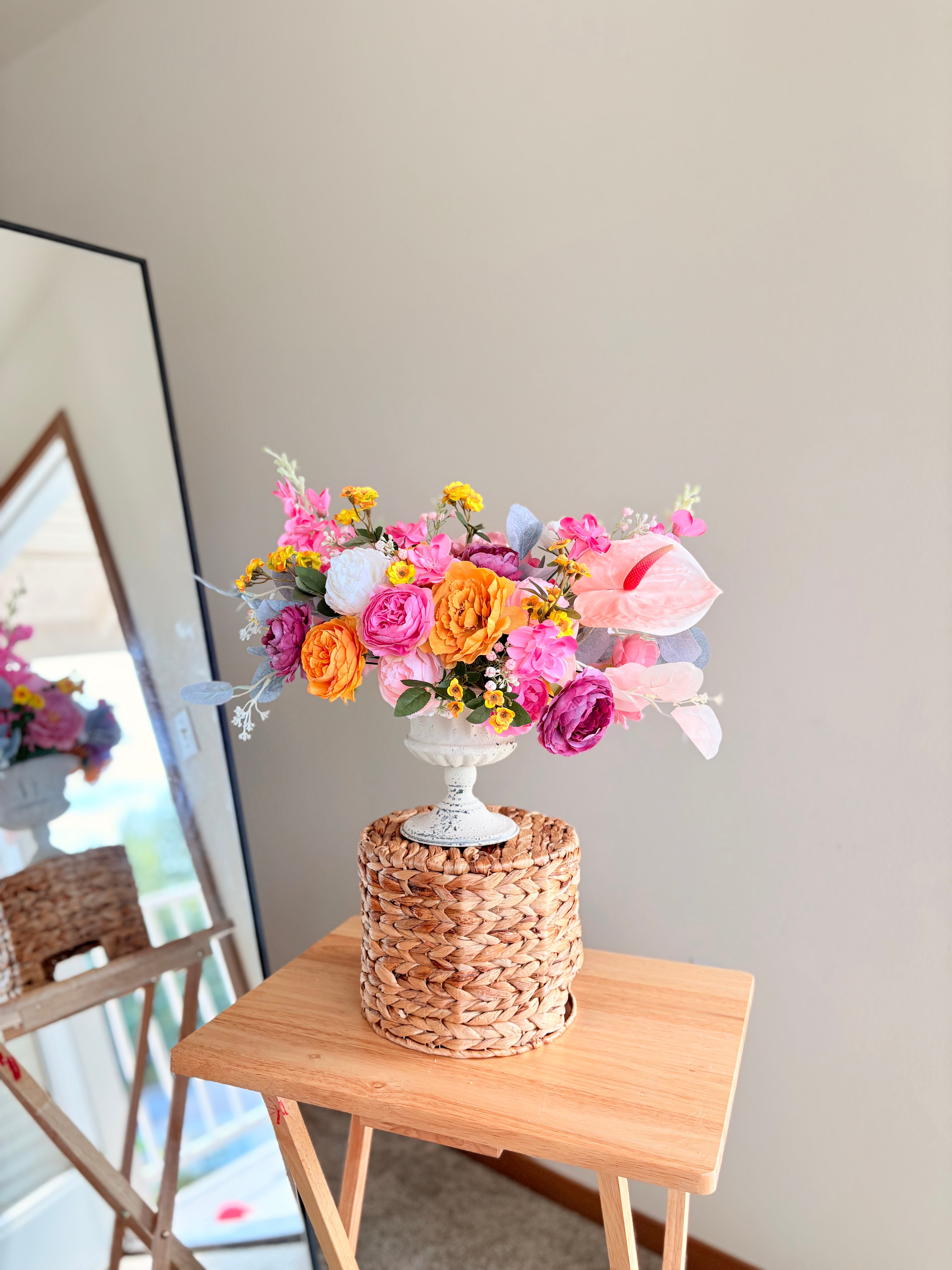 Colorful flower arrangement in a woven basket on a wooden table against a neutral wall.