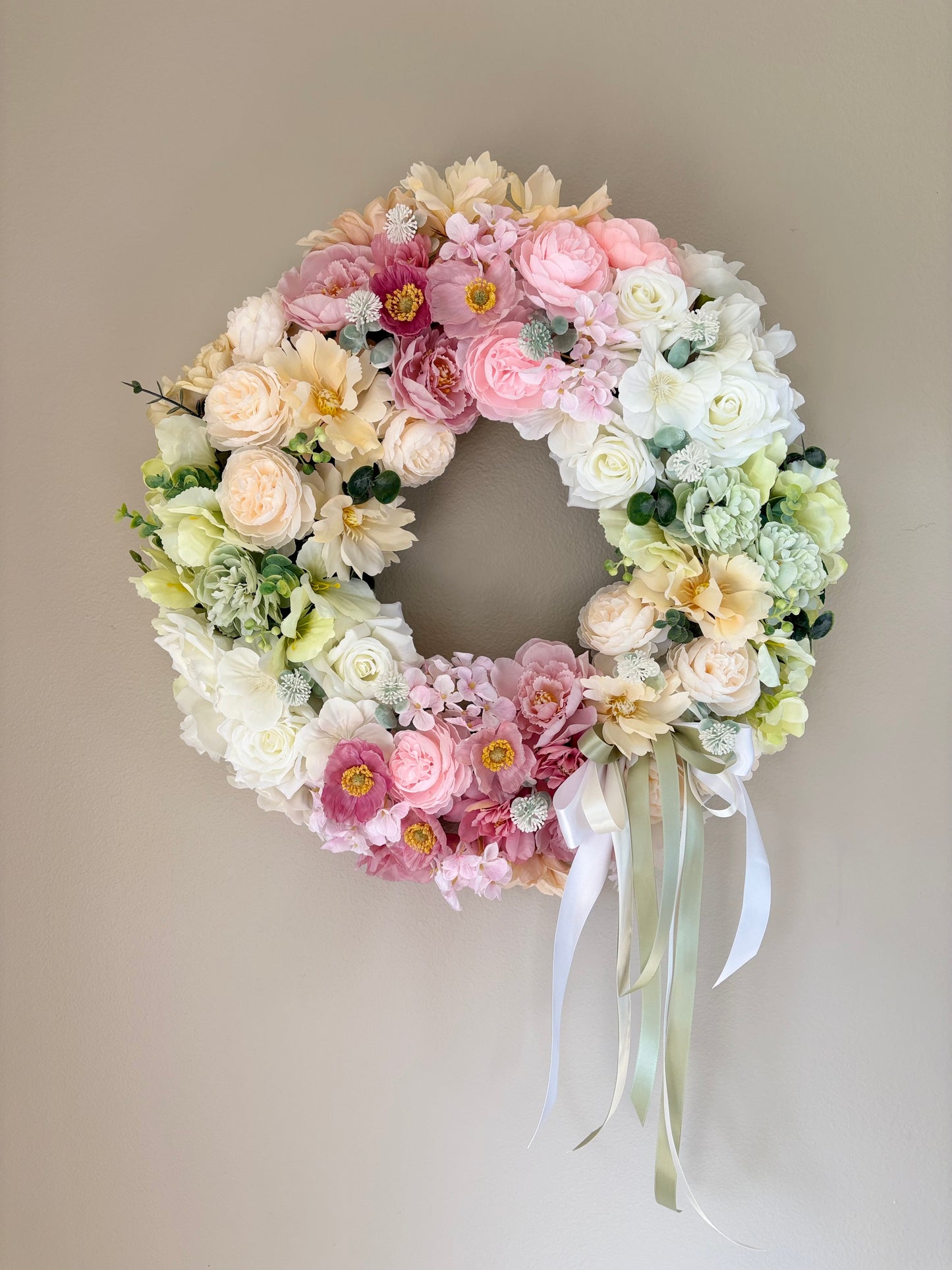 Floral wreath with pastel flowers and ribbons on a plain background