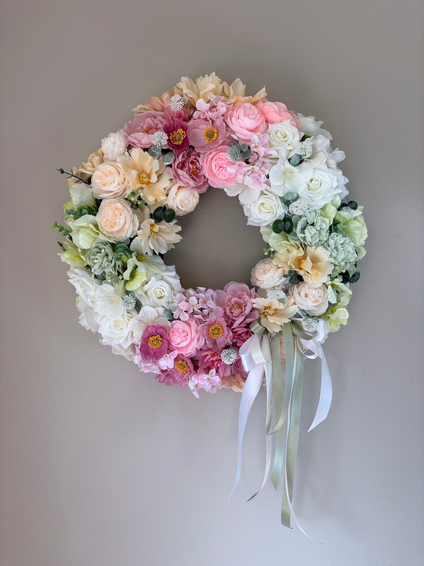 Floral wreath with pink, white, and green flowers on a plain background