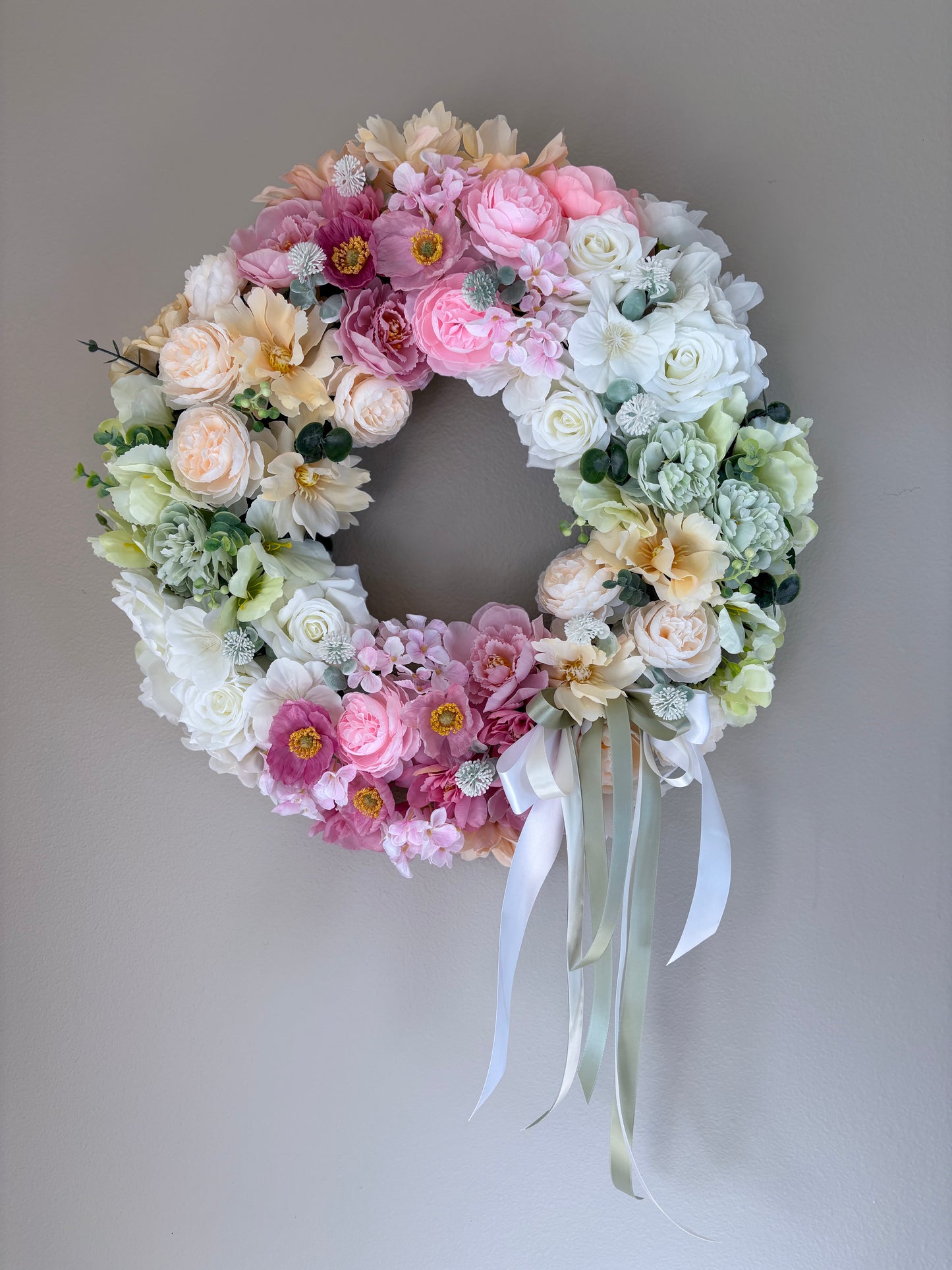 Floral wreath with pastel flowers and ribbons on a plain background
