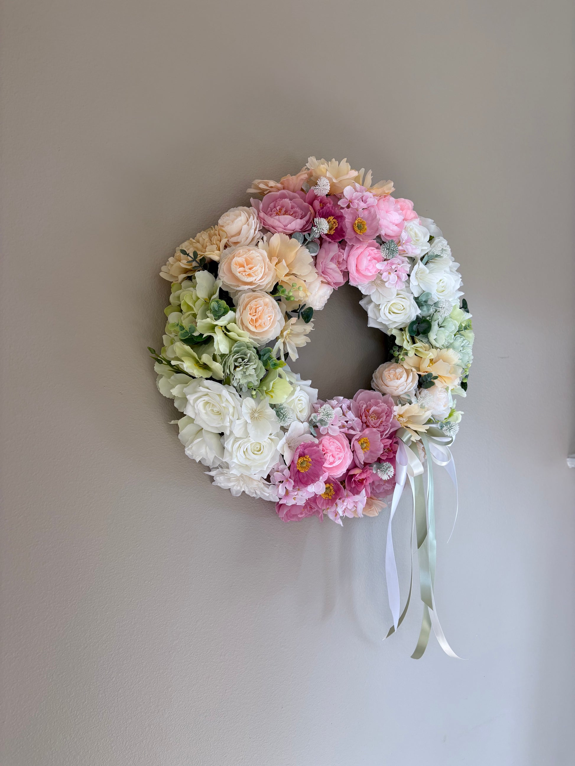 Floral wreath with pink, white, and green flowers on a plain wall.
