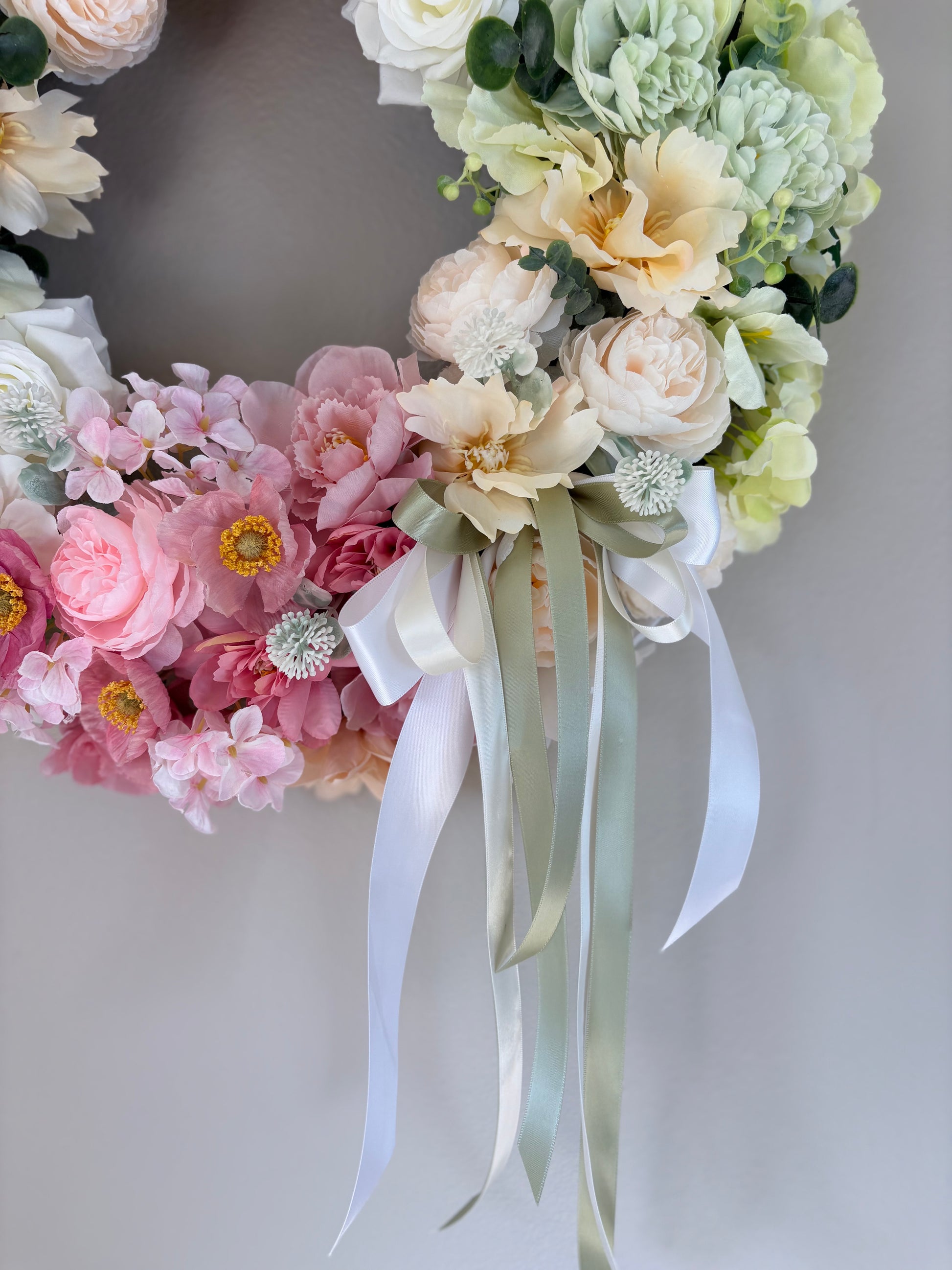 Floral wreath with pastel flowers and ribbons on a plain background