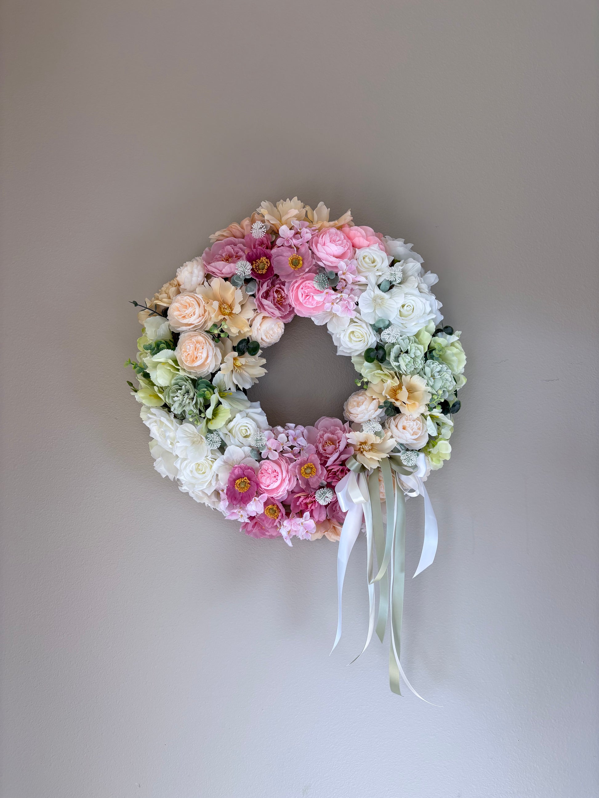 Floral wreath with pink, white, and green flowers on a plain wall.