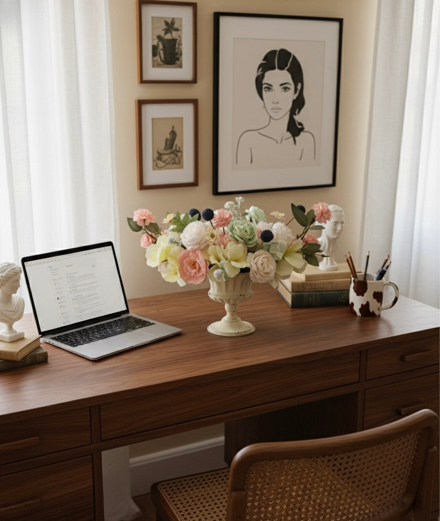Home office desk with laptop, flowers, and framed art on a wall.