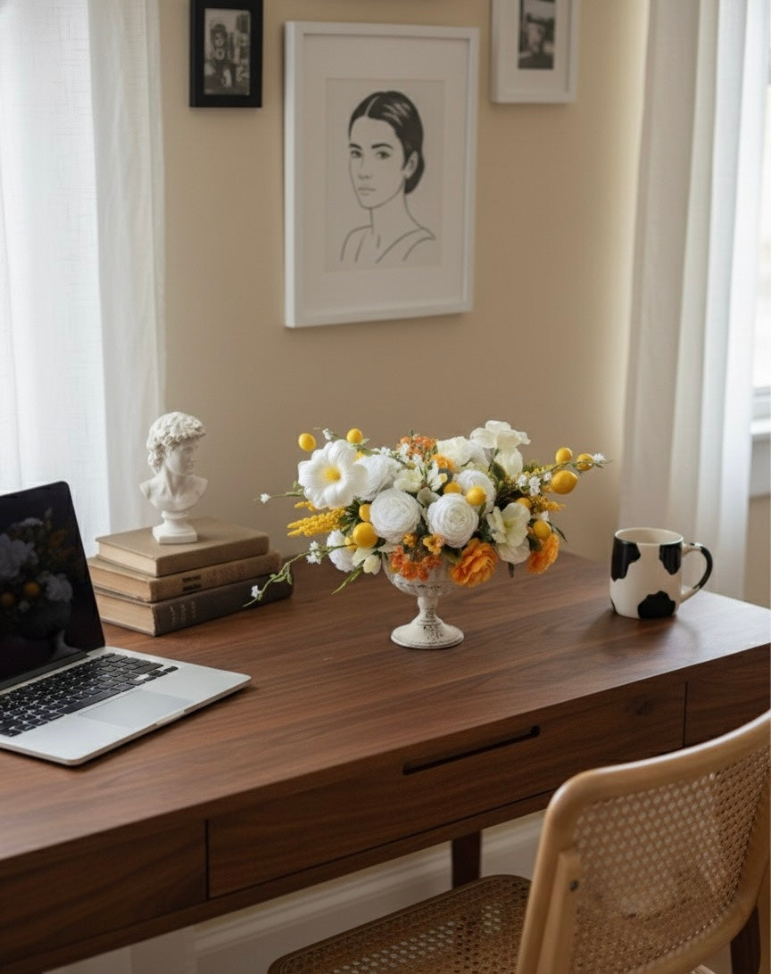 Home office desk with laptop, mug, books, and flowers on a wooden desk.