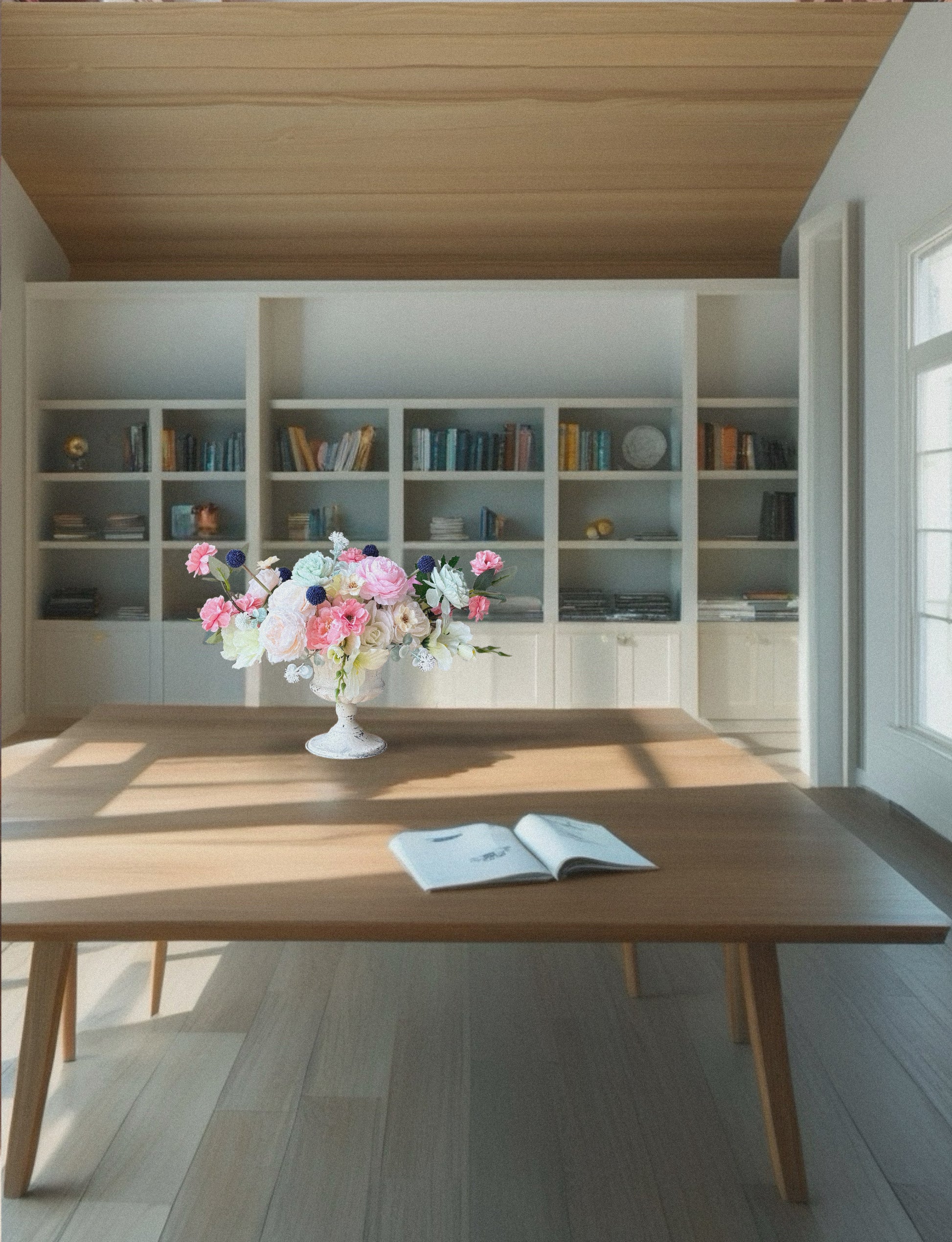 Wooden table with a vase of flowers and an open book in a room with shelves and books.
